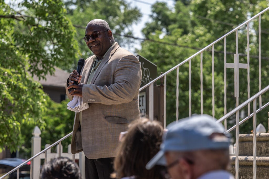  Reverend Anthony Talton speaking into a microphone while standing on the church steps