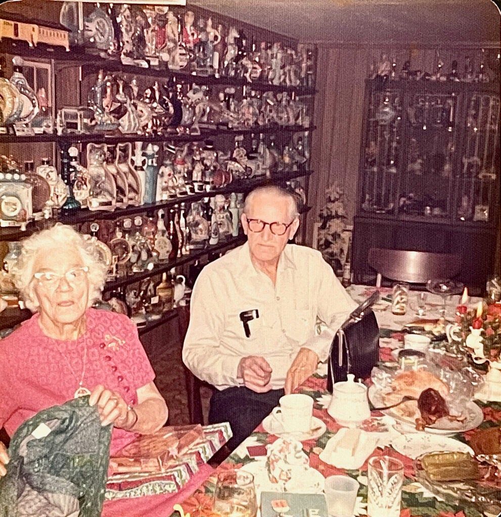 Uncle Henry sitting ata table with his decanter collection on the wall behind him