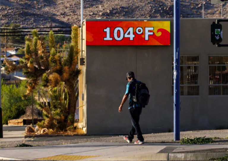 A man walking outside with a digital sign showing temperature is 104 degrees