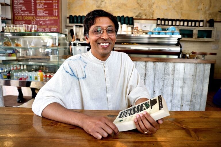 Nikil Saval posing for a photo in a coffeeshop with the book 'Ulysses'