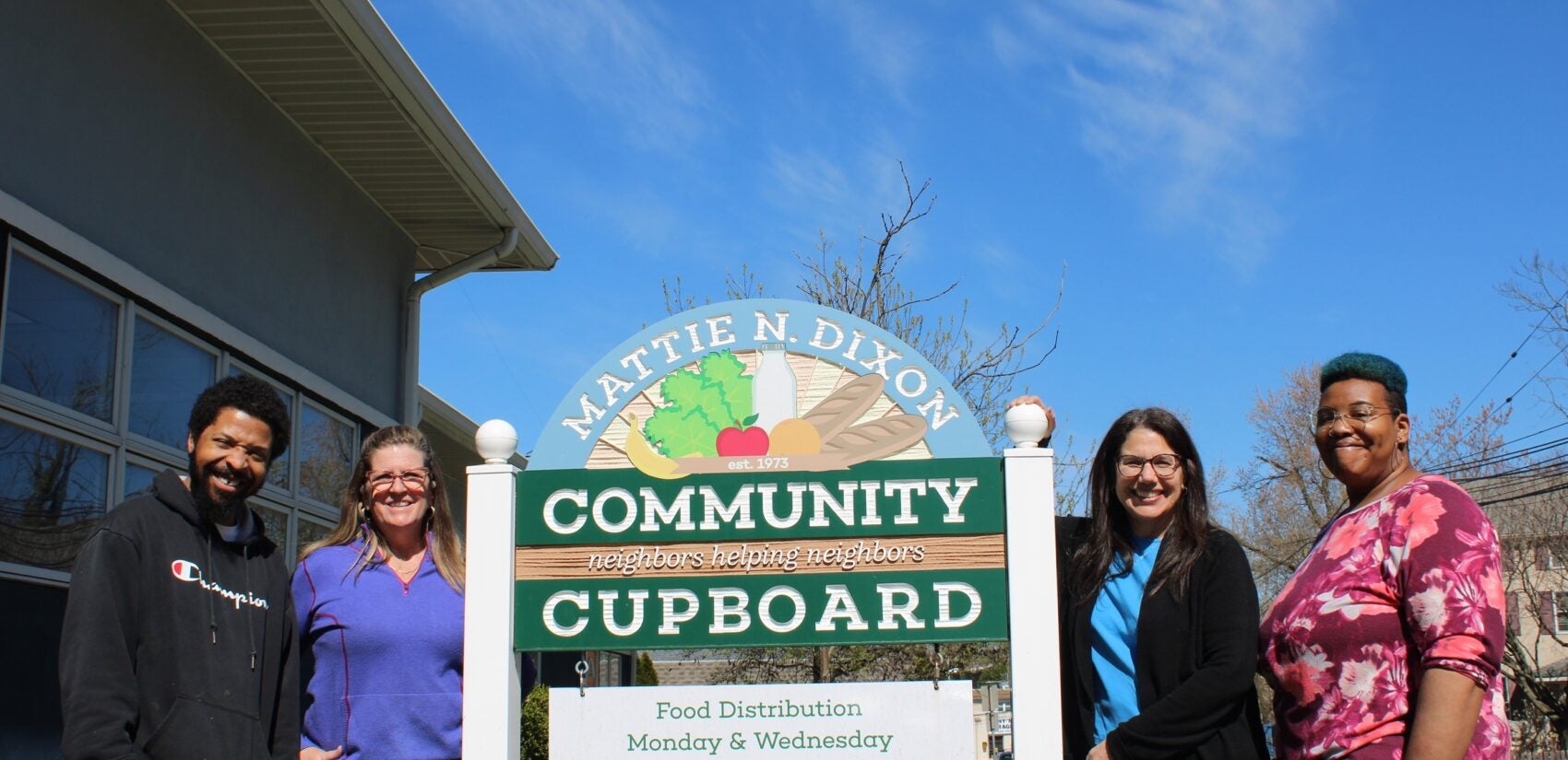 Staff members and volunteers stand by a sign for Mattie N. Dixon Community Cupboard