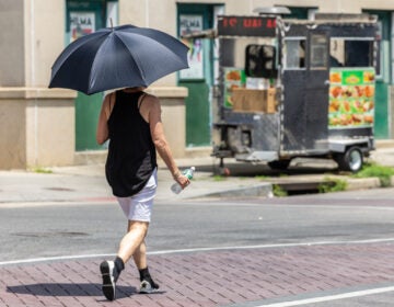 A person walkng down the street with an umbrella to get out of the sun