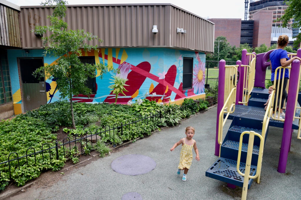 Two small children and a woman play on a playground near a colorful mural painted on a building's wall