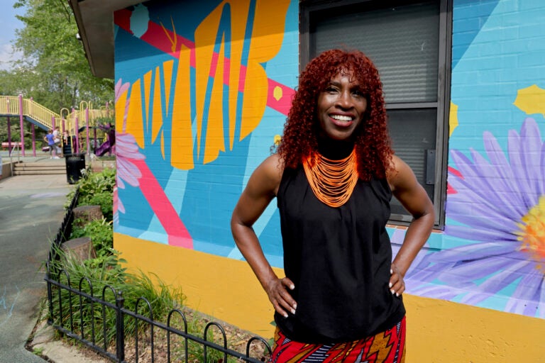 A woman with red hair stands in front of a wall with a painted mural