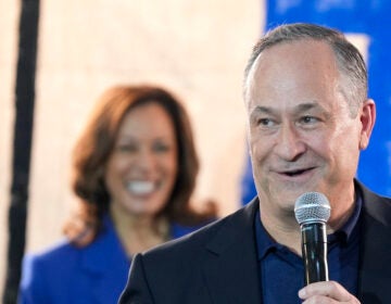 Doug Emhoff speaking into a microphone as Kamala Harris watches