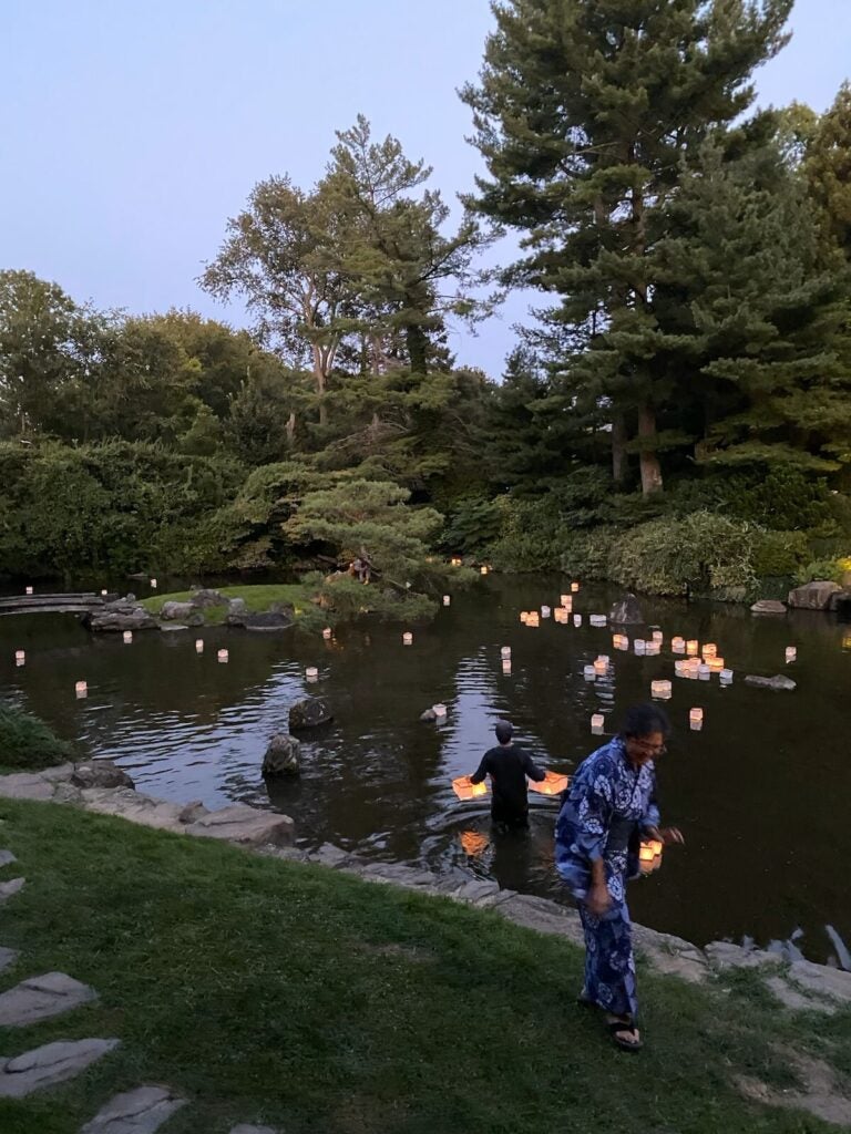 Paper lanterns float on a body of water with two people in the foreground