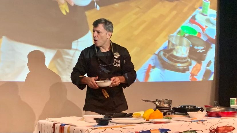 A man makes meals out of insects on stage at Drexel University's Academy of Natural Sciences