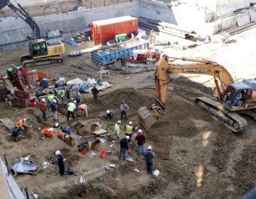 Workers with machines excavate coffins from a construction site in the Old City