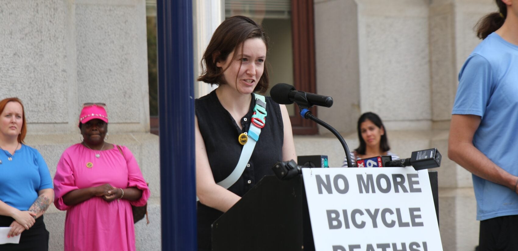 Julie White speaks at a podium with a sign reading NO MORE BICYCLE DEATHS