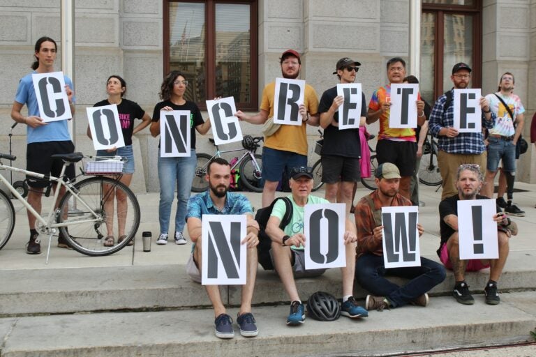 Cyclists and activists hold signs, one big one reading CONCRETE NOW!