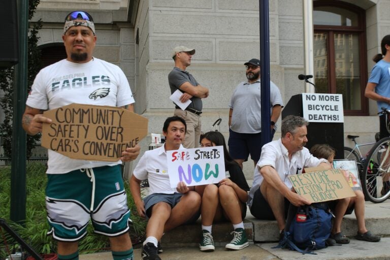 Activists hold multiple signs, one reading COMMUNITY SAFETY OVER CAR'S CONVENIENCE