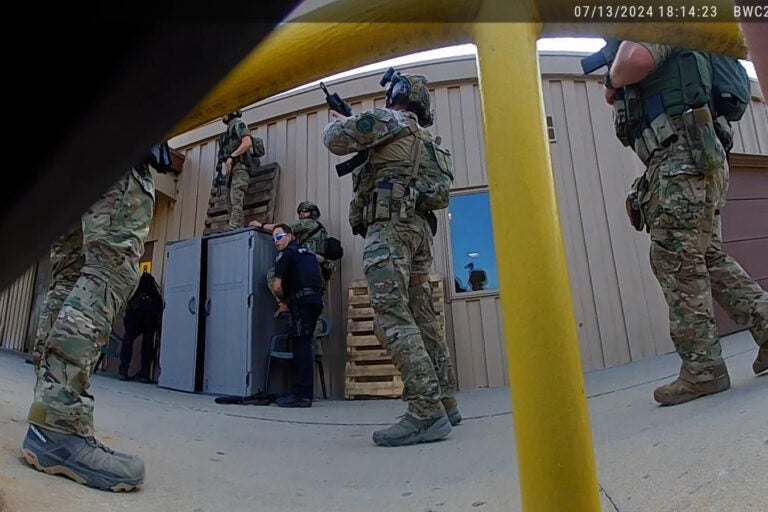 One officer gestures to his colleague to hoist him up onto a roof