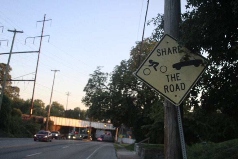 a sign on Chester Pike reads Share the Road and has symbols for a cyclist and car