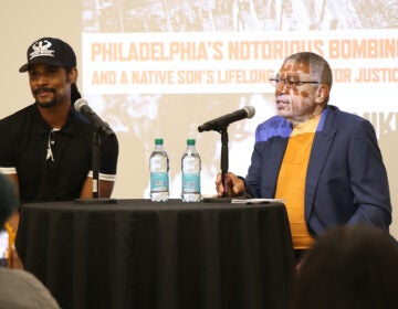 Linn Washington Jr. and Mike Africa sit at a table with a microphone and water bottles