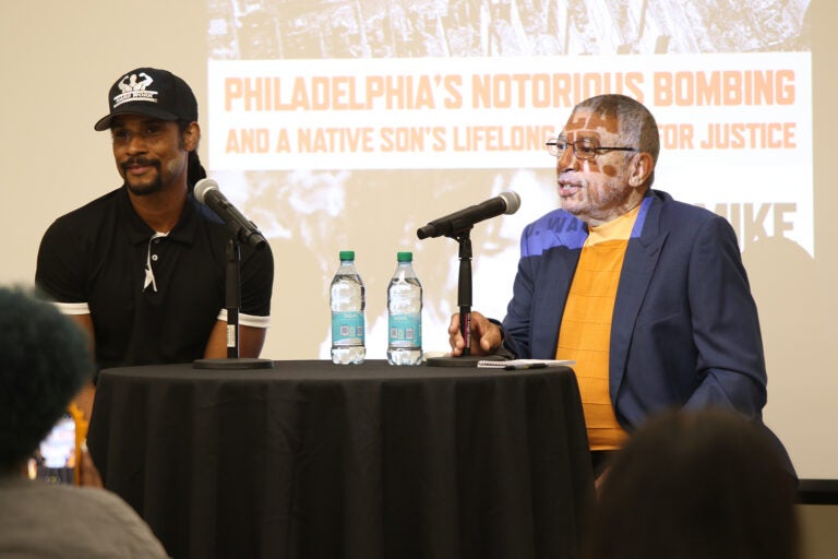 Linn Washington Jr. and Mike Africa sit at a table with a microphone and water bottles