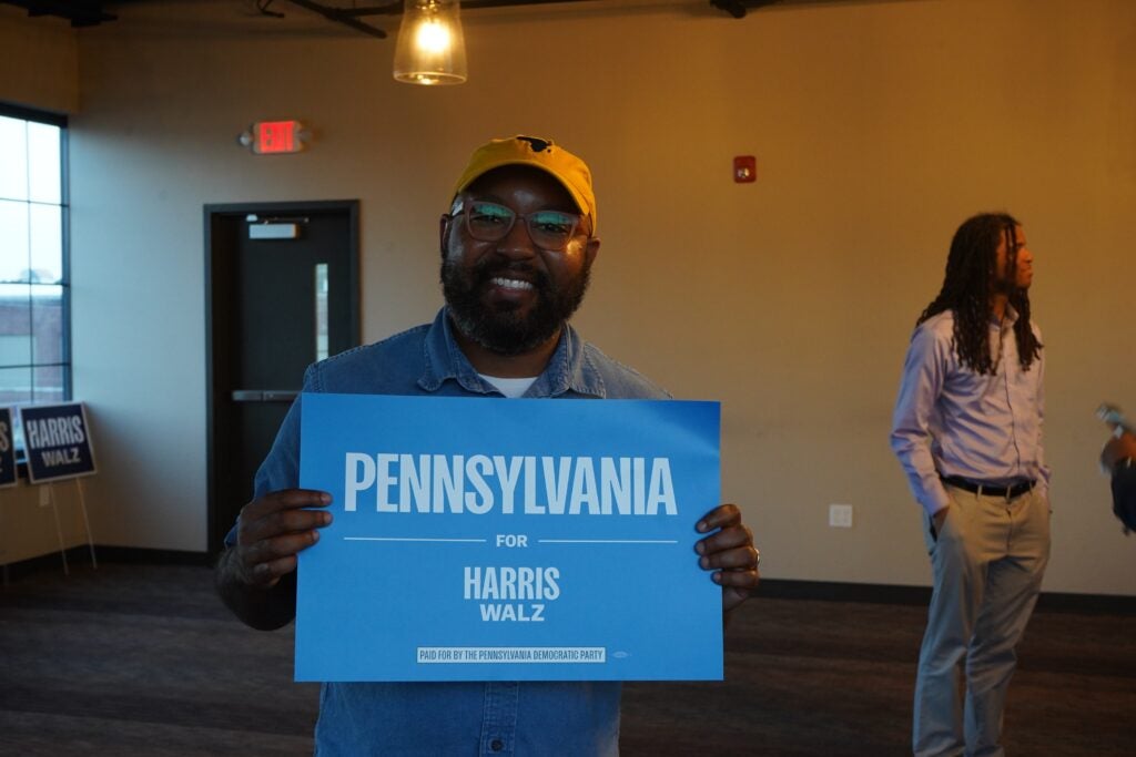 Greg Scott holds a sign reading Pennsylvania for Harris Walz