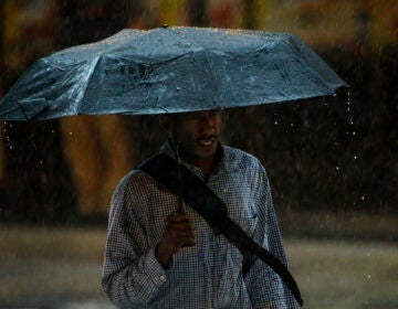 A man walks under an umbrella during a rain storm, Tuesday, July 15, 2014, in Philadelphia