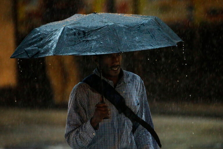 A man walks under an umbrella during a rain storm, Tuesday, July 15, 2014, in Philadelphia