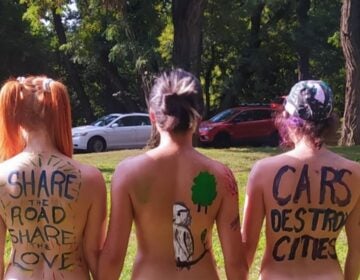 3 topless women with their backs to the camera with messages painted on themselves