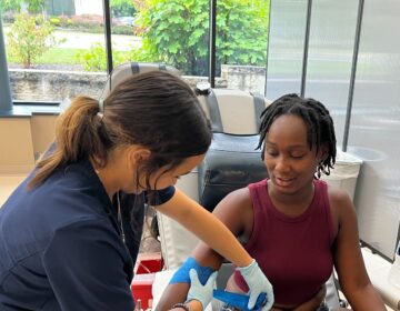 A woman ties a bandage around another woman's arm as she prepares to give blood