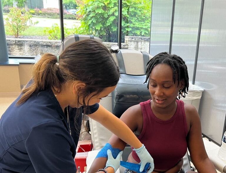 A woman ties a bandage around another woman's arm as she prepares to give blood