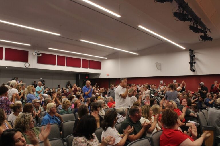 More than 500 people pack an auditorium for the board meeting. Attendees often interrupted speakers at the microphone throughout the evening, booing and shouting.