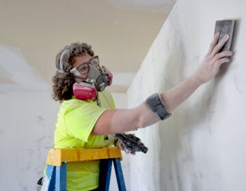 A person wearing a gas mask works on a home