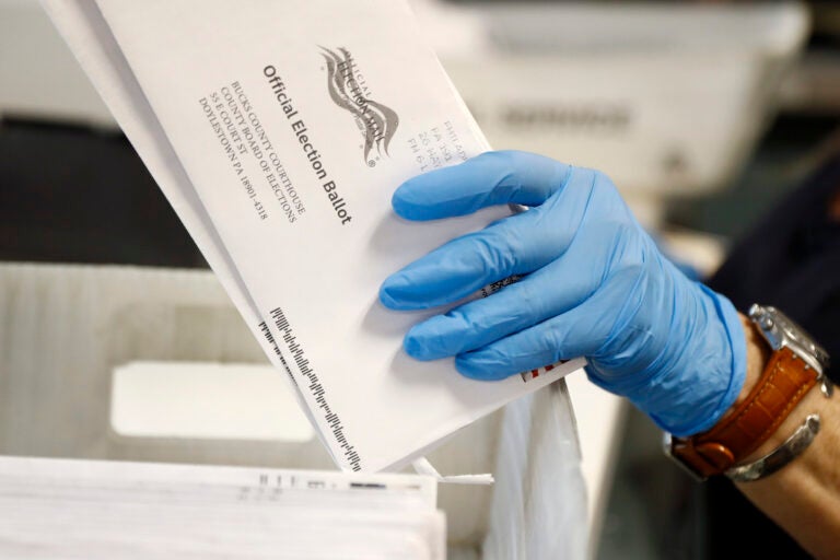 a hand holds mail-in ballots