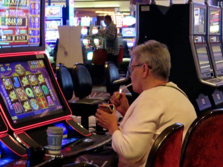 Someone lights a cigarette while playing a slot machine in a casino