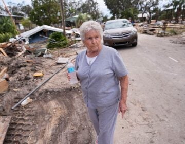 Elsie Hicks walks with a water bottle among storm damage