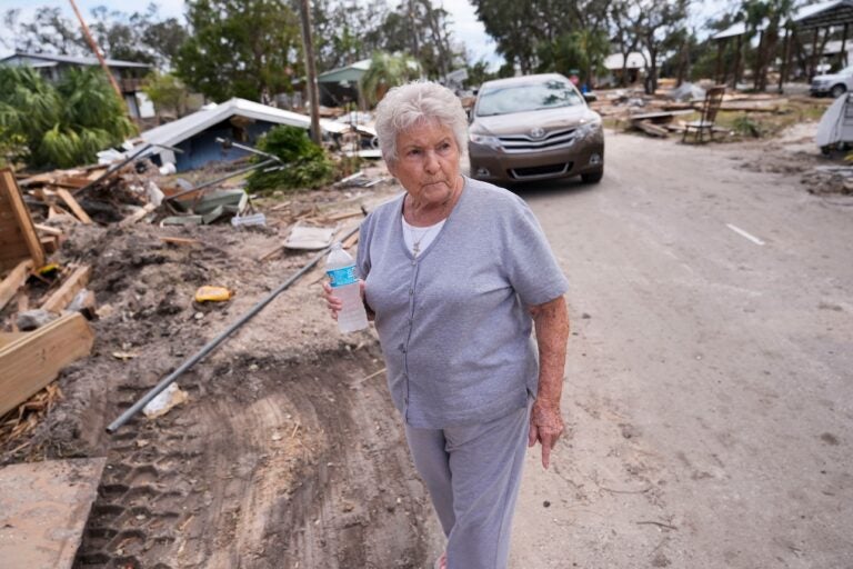 Elsie Hicks walks with a water bottle among storm damage