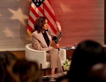 Kamala Harris raises her hand while sitting holding a microphone