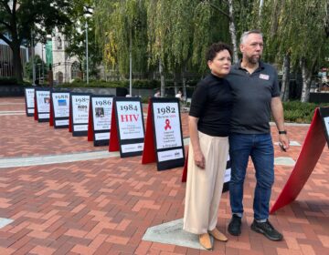 Robb Reichard of AIDS Fund and Eveyln Torres of Action Wellness stand in front of the 1981 - Until It’s Over Timeline. Double sided boards track the history of the AIDS epidemic to educate student passersby. (Lily Cohen/WHYY)