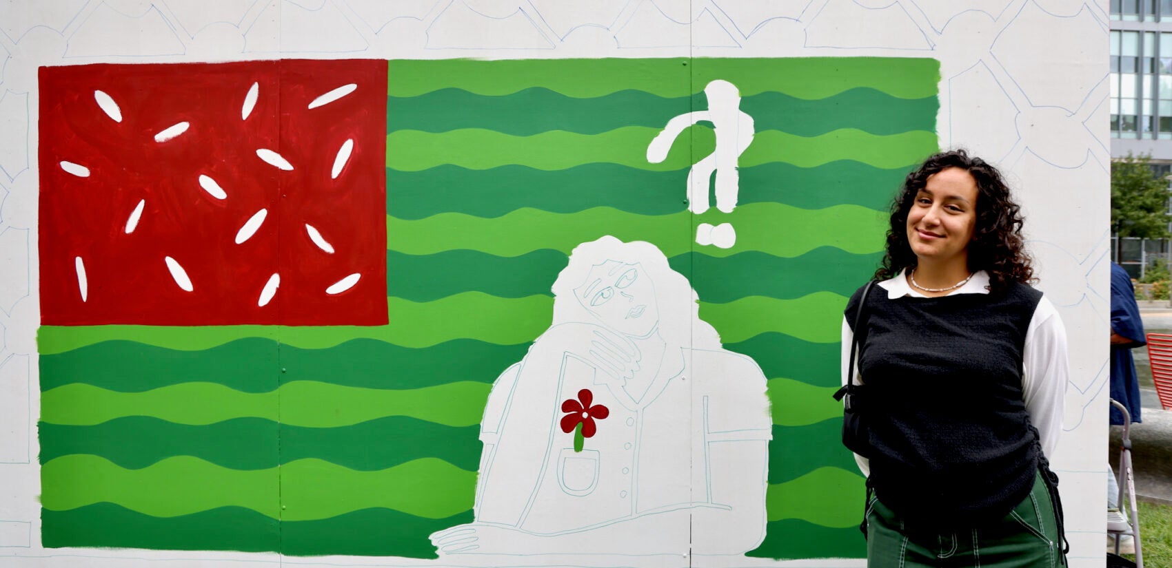 Woman stands in front of a unfinished mural of the American flag painted with watermelon colors