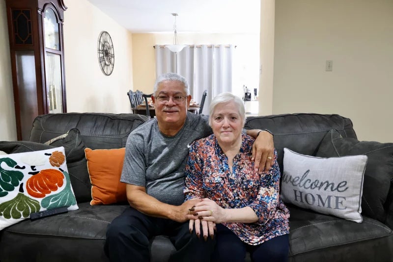 Miriam Saladin and her husband, Benny, sit in a couch and hold hands