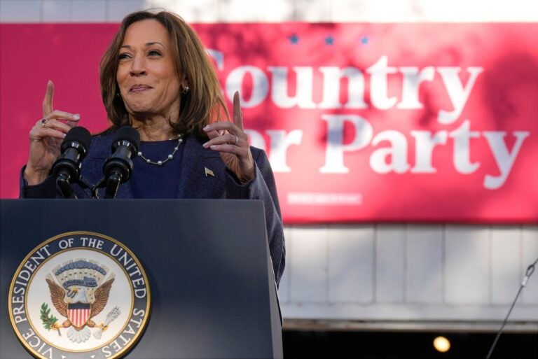 Kamala Harris speaks behind a podium and in front of a sign reading Country Over Party