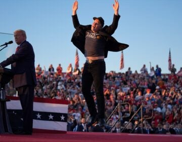 Elon Musk jumps in the air next to Donald Trump onstage