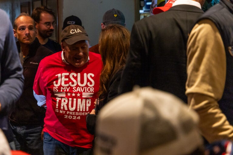 a man wears a shirt reading JESUS IS MY SAVIOR, TRUMP IS MY PRESIDENT 2024 and a CIA hat