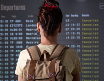 A young woman is looking at cancelled flights on a departure screen at an airport. (Bigstock/xavigm)