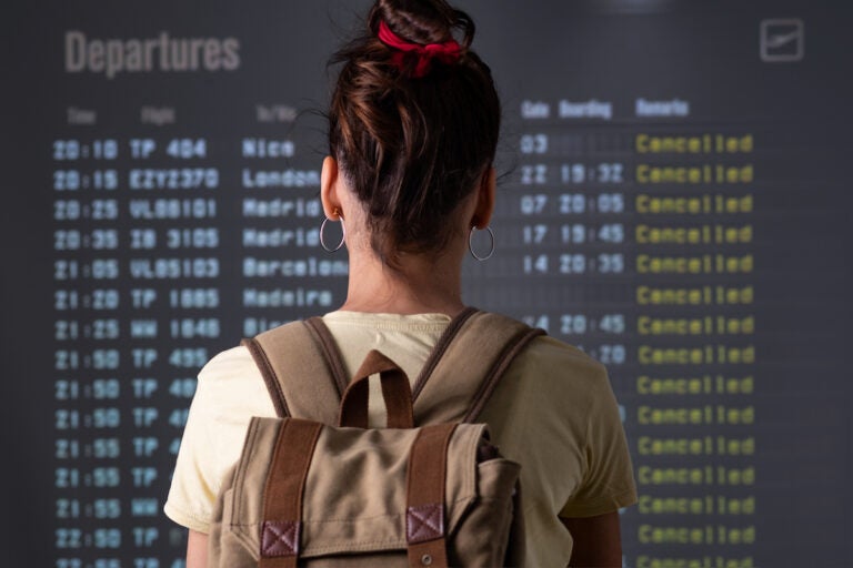 A young woman is looking at cancelled flights on a departure screen at an airport. (Bigstock/xavigm)