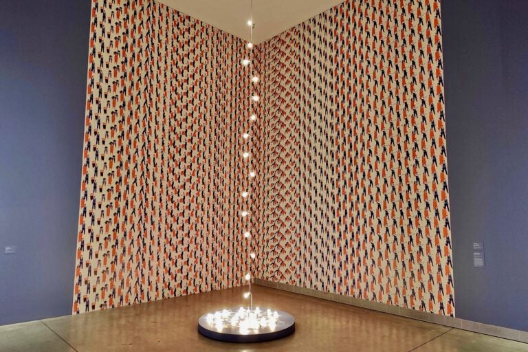 Felix Gonzalez-Torres' light sculpture, ''Untitled (Petit Palais)'' (1992) was inspired by the death of his partner Ross Laycock from AIDS.  It is set against Nick Cassway's wallpaper, ''Above the Sound of Ideologies Clashing.'' (Peter Crimmins/WHYY)