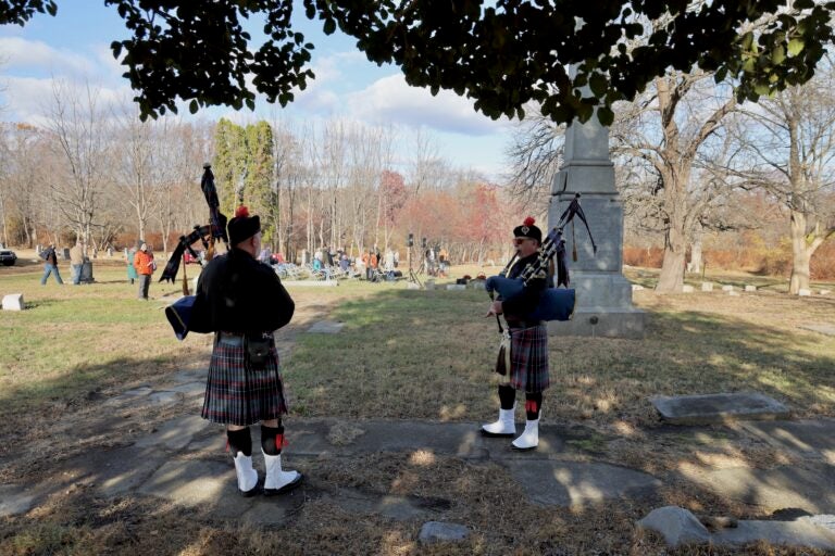 John Ginty and David Hollinger, of the Philadelphia Police and Fire Pipes and Drums, pipe a prelude to a service commemorating the reburial of hundreds of remains uncovered during construction on Arch Street. (Emma Lee/WHYY)