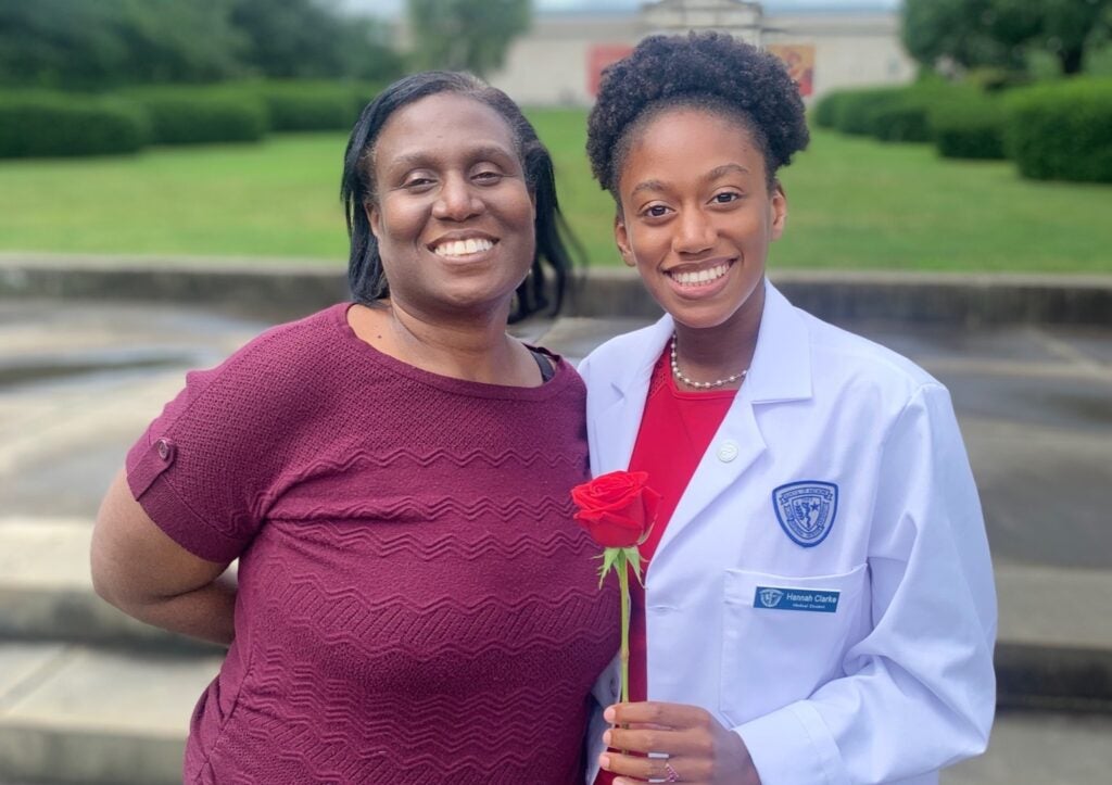 Hannah and Claudine Clarke smile with Hannah wears a white coat and holds a rose