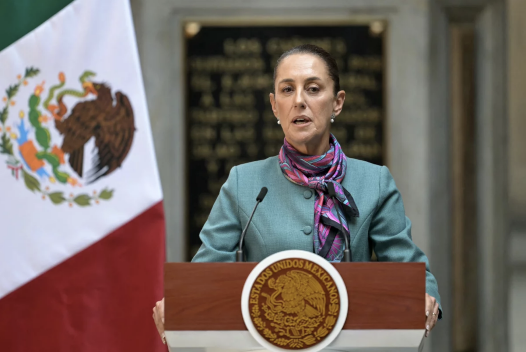 Claudia Sheinbaum speaking at a podium with the Mexican flag behind her