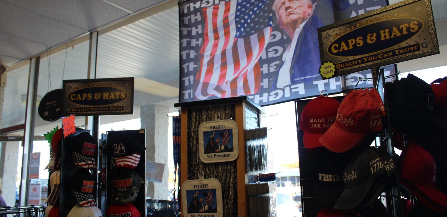 MAGA hats in front of a flag of Trump raising his fist directly after the assassination attempt