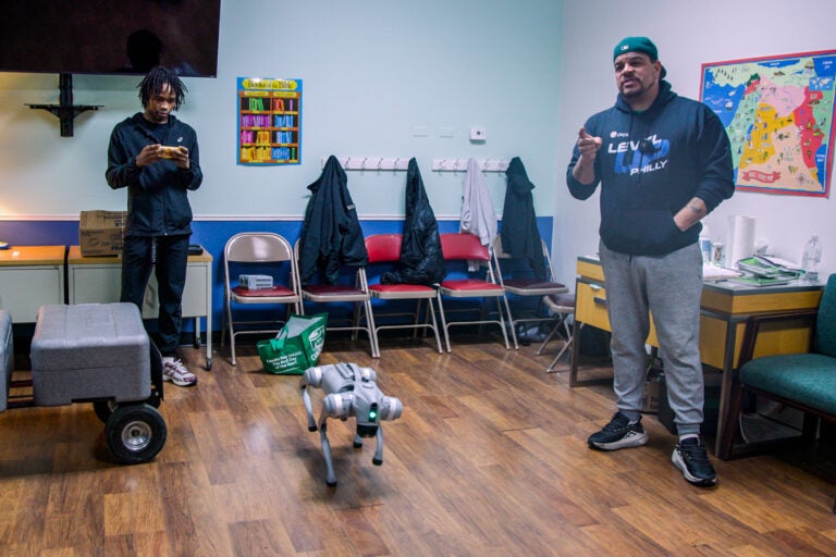 Aaron Campbell speaks next to Sybir Brown and a robotic dog