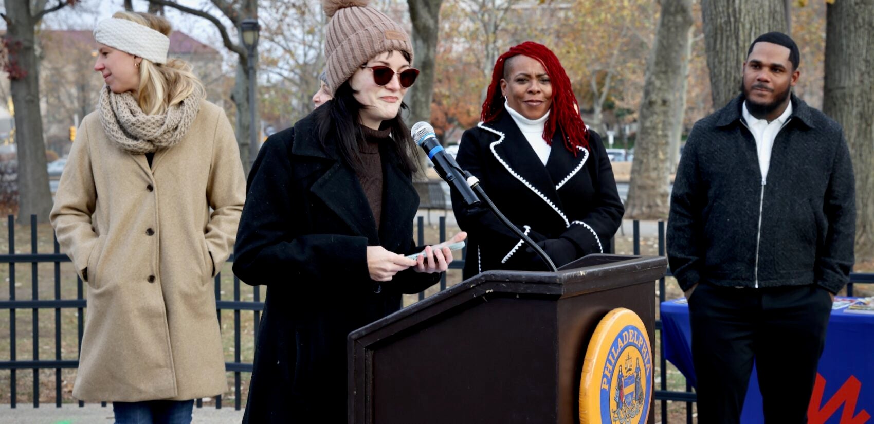 Ash Ryan speaking at a podium at a press conference