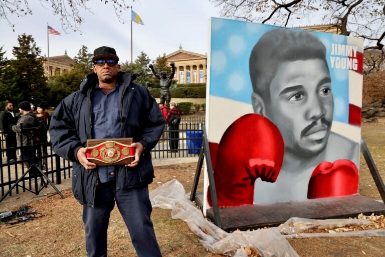 Jason Young posing in front of the large portrait of Jimmy Young with his boxing gloves