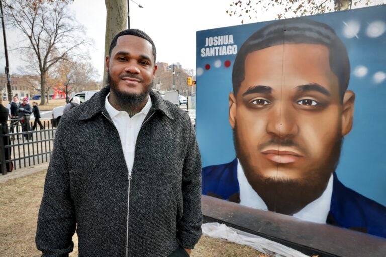 Joshua Santiago posing for a photo in front of a large portrait of him