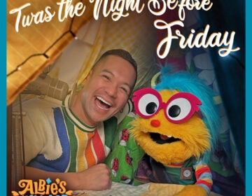 Image of a smiling person in a colorful sweater next to a vibrant yellow puppet with bright blue hair, red glasses, and a cheerful expression. The text 'Twas the Night Before Friday' is displayed in a whimsical font at the top, with the logo 'Albie's Elevator' in the corner.